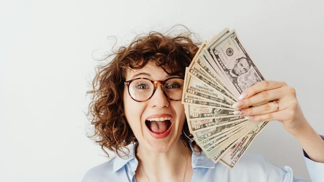 Caucasian woman with curly hair delights in holding US dollars against a white background.