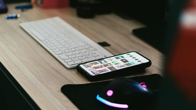 A sleek desktop setup featuring a smartphone, keyboard, and vibrant RGB mouse.