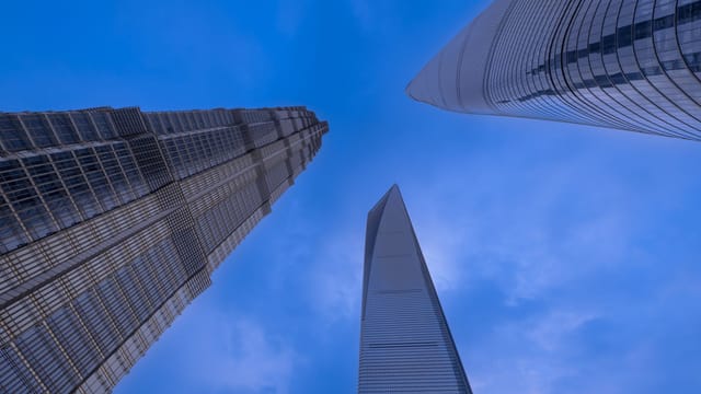 Low angle view of iconic skyscrapers in Shanghai against a vibrant blue sky.