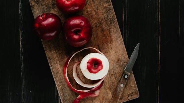 Close-up of red apples with peeling knife on wooden board, ideal for food themes.