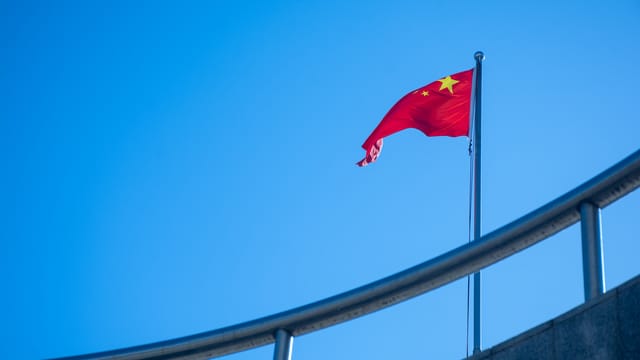 The Chinese national flag waving against a clear blue sky, symbolizing patriotism.