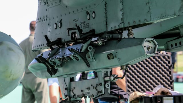 Detailed view of a military aircraft machinery component with people in the background.