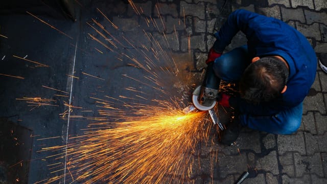 A technician uses a grinder to shape metal, causing vibrant sparks in a workshop.