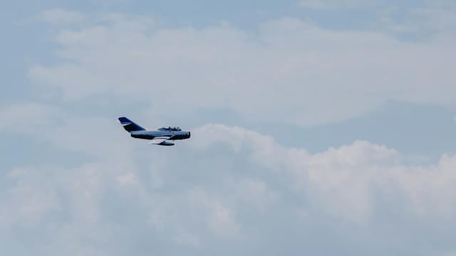 Creative design of modern fighter aircraft flying in light sky with fluffy clouds in daylight