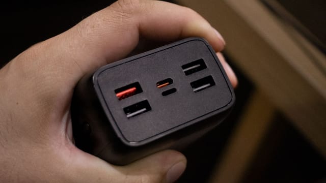 Close-up shot of a hand holding a multi-USB port power adapter, highlighting its ports.