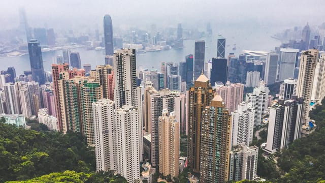 Aerial view of skyscrapers on Hong Kong Island with a misty harbor backdrop.