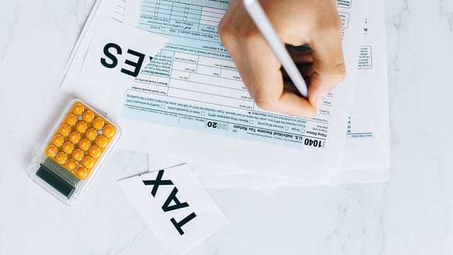 Close-up of hand writing on tax form with calculator nearby on white surface.