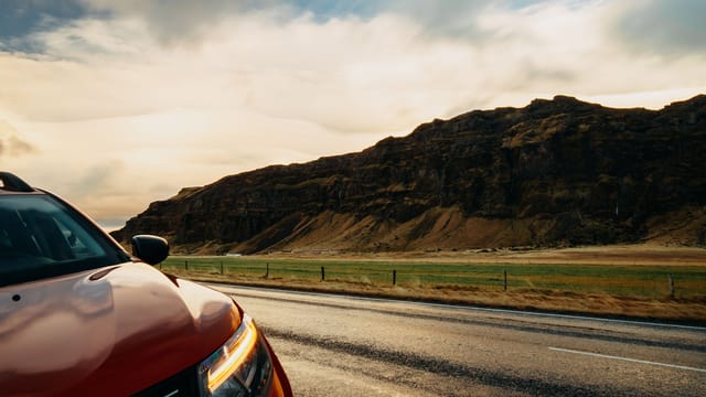 Illustrative image: A red SUV travels along a rural road with a picturesque mountain landscape under a bright sky.