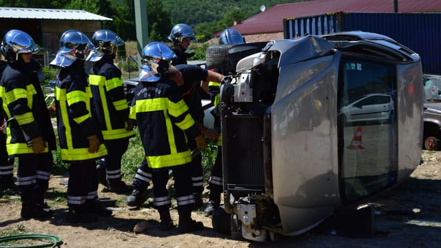 Firefighters attending to an overturned vehicle at an accident scene. Daylight outdoor operation.