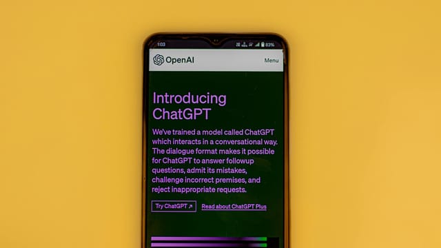 Mobile phone displaying the ChatGPT introduction screen with OpenAI branding on a yellow background.