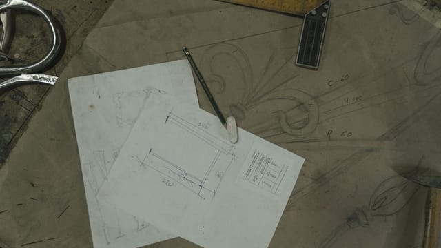 Detailed view of architectural sketches and drawing tools on a workbench, reflecting a crafting workspace.