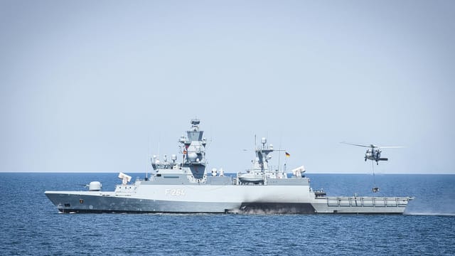 A naval frigate navigates open waters with a hovering helicopter, showcasing maritime operations.