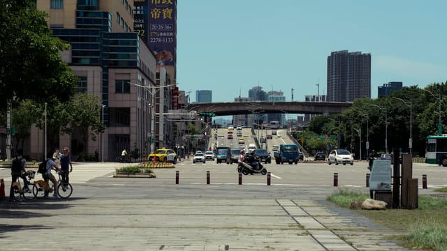 Busy street scene in Taipei with cyclists, cars, and urban buildings under clear sky.