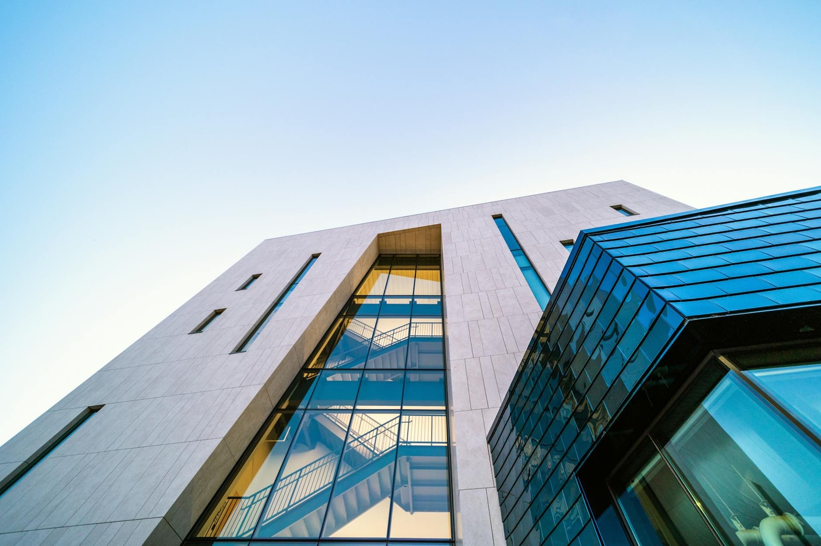 From below of modern geometric building with glass details and staircase inside against cloudless blue sky