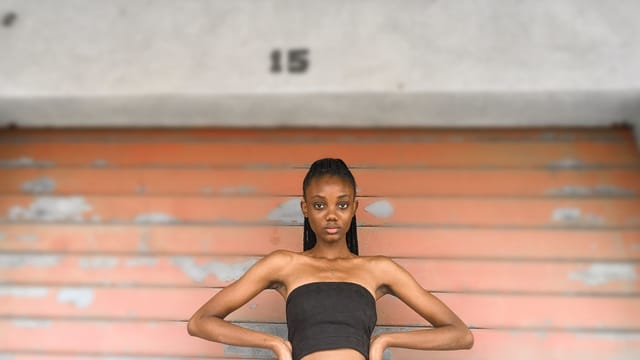 An adult woman confidently poses in a black tube top against a textured background.