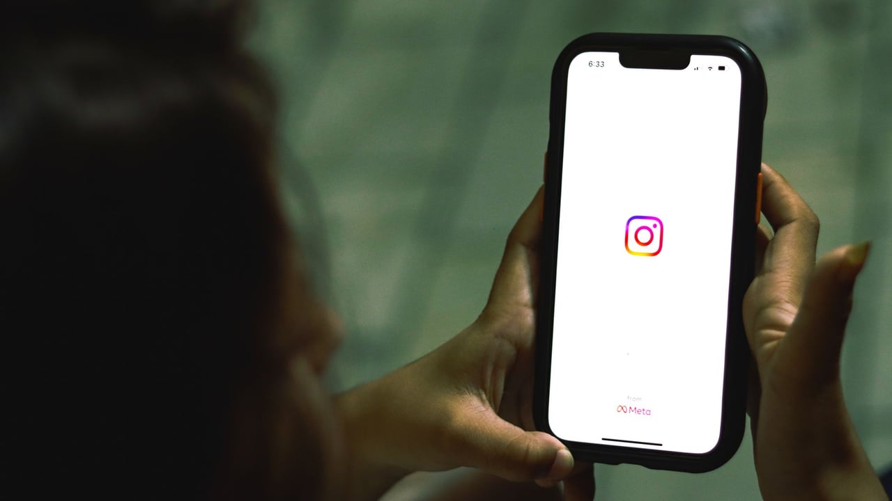 Close-up of a woman holding a smartphone displaying the Instagram app indoors.