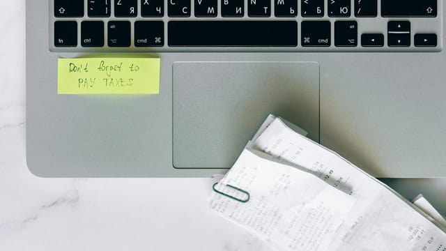 A laptop with a sticky note reminder and receipts, emphasizing tax season organization.