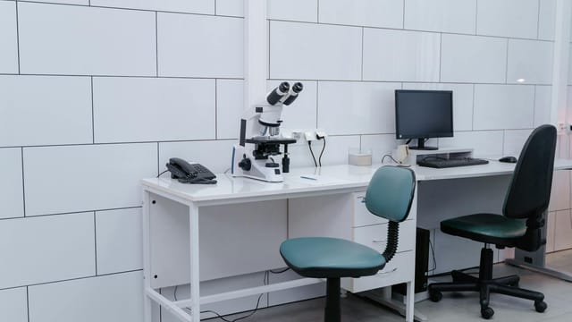 Modern laboratory with microscope, monitor, and office equipment on desk.