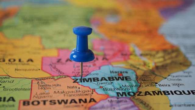 A blue pushpin marks Zimbabwe on a colorful close-up map highlighting its geographical position.