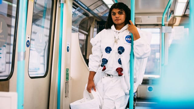 A person in an astronaut costume rides the London subway, blending futuristic themes with urban commute.