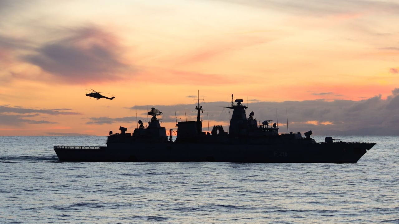 Silhouette of a warship and helicopter at sea during sunset.