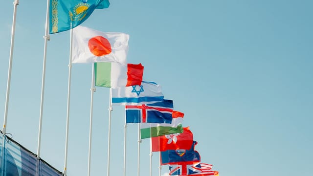 A row of international flags waving under a clear blue sky in Paris, France.