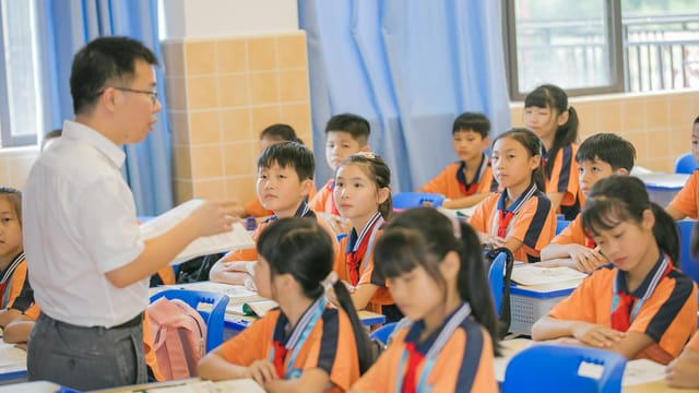 Asian teacher conducting a lesson with attentive students in a bright classroom setting.