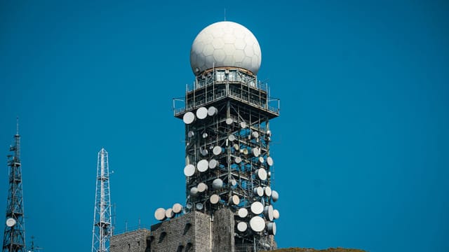 Imposing satellite tower with numerous dishes against a vibrant blue sky.