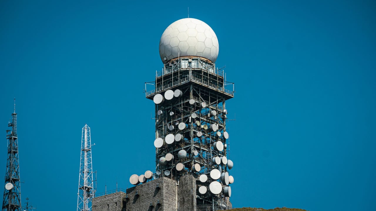 Imposing satellite tower with numerous dishes against a vibrant blue sky.