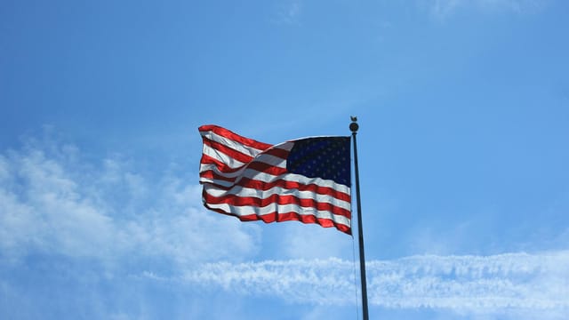 American flag waving on a flagpole against a clear blue sky in New York.