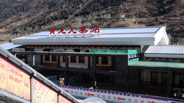 A contemporary train station set against a scenic mountainous backdrop under clear skies.