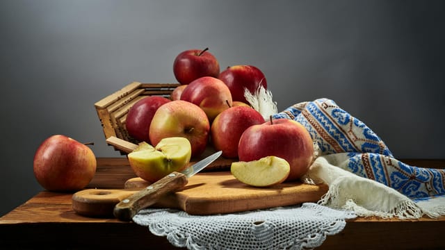 A captivating still life arrangement featuring fresh apples, a knife, and a rustic cloth on a wooden table.