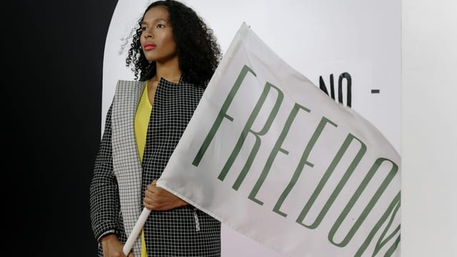 A woman with curly hair holding a Freedom flag indoors. Modern and powerful imagery.