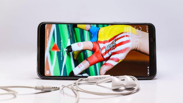 Smartphone displayed with wired earphones, featuring colorful screen on a white background.