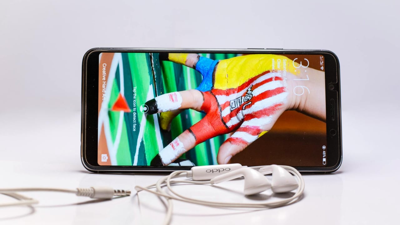 Smartphone displayed with wired earphones, featuring colorful screen on a white background.
