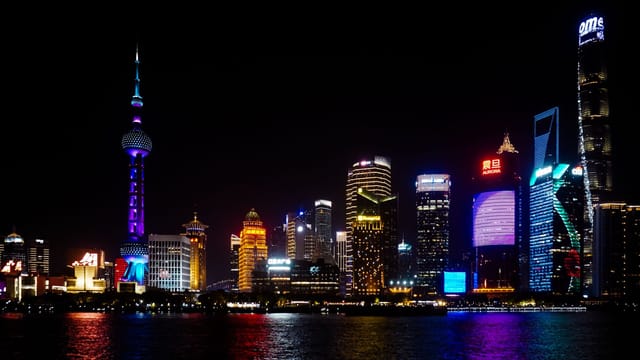 Illustrative image: Vibrant Shanghai skyline at night featuring iconic skyscrapers and colorful lighting reflections on water.