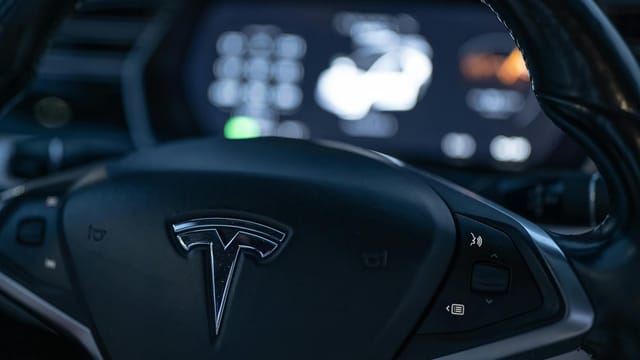 Detailed view of a Tesla steering wheel with dashboard display in focus, showcasing modern car interior design.