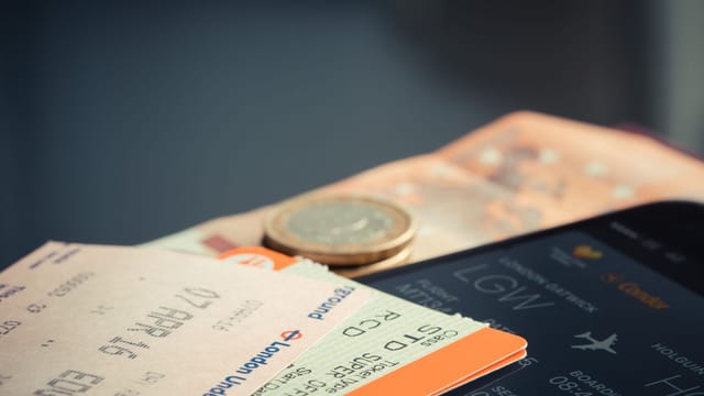 Airline ticket with euro coins and smartphone displaying flight details.