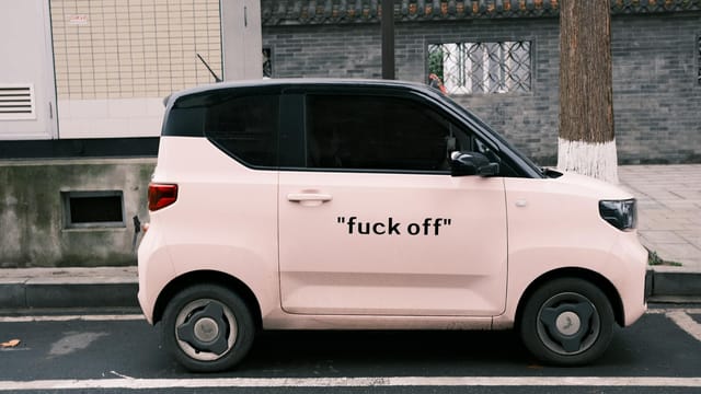 Side view of a pink compact electric vehicle parked on an urban street with bold text on the side.