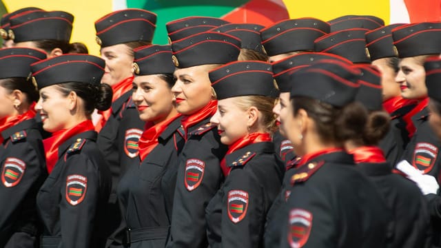 Group of female cadets in formal uniforms participating in an outdoor ceremony on a sunny day.