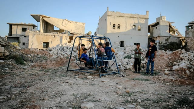 Syrian children play on a swing amidst the decaying ruins of Idlib after conflict.