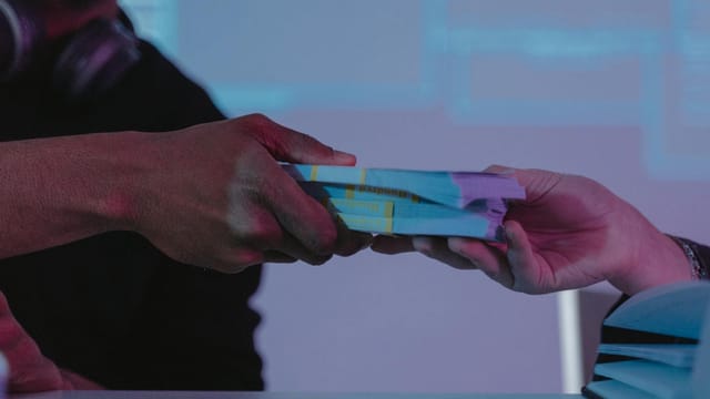 Close-up of hands exchanging money, highlighting financial exchange in a dimly lit setting.