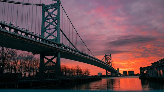 A stunning sunset view of the Benjamin Franklin Bridge in Philadelphia, with vivid orange and purple skies.