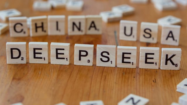 Wooden letter tiles spelling "DEEPSEEK" with "CHINA" and "USA" on a wooden table.