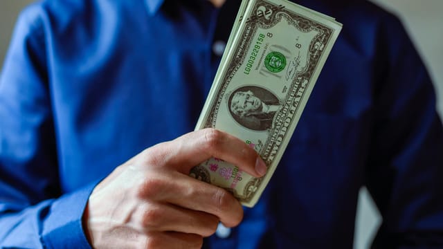 Close-up of a person holding two dollar bills, representing wealth and finance.