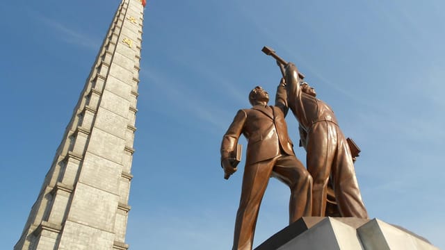 Low angle view of Juche Tower and worker statues against a clear blue sky in Pyongyang, North Korea.