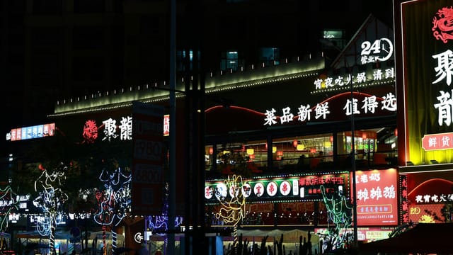 Colorful neon-lit street market bustling with nightlife and Chinese signage.
