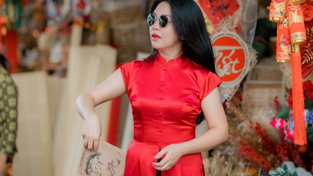 Elegant woman in a red cheongsam holding a fan, celebrating the Lunar New Year festivities.