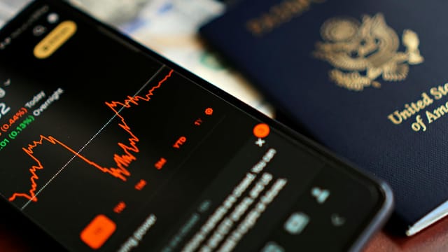 Close-up of a smartphone displaying stock data next to a US passport, suggesting travel and finance themes.