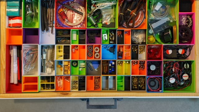 Top view of a neatly organized drawer filled with colorful containers holding various tools and electronic parts.
